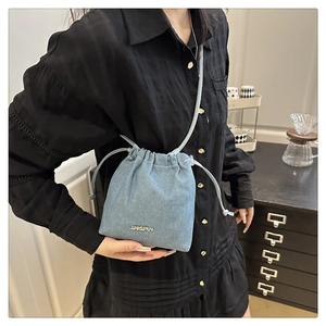 Detail of light blue denim bucket bag with drawstring and metal logo on casual outfit