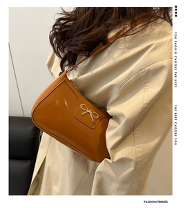 Detail of caramel glossy patent leather shoulder bag with gold bow ornament and smooth texture