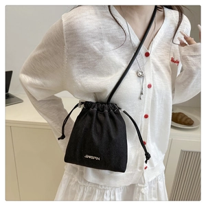 Mini black drawstring bucket bag with silver logo worn by model in a modern room