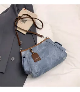 Detailed view of blue denim crossbody bag featuring brown leather trim and side flap pockets