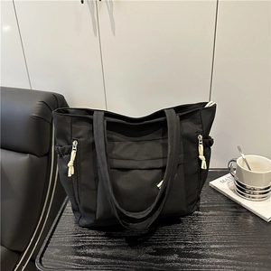 Black large capacity nylon tote bag with multi-pocket design on a dark wood surface