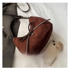 Detail of dark brown suede tote bag with a decorative bow on a white textured background