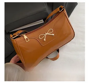 Detail of glossy brown baguette bag with golden metal bow and premium faux leather texture