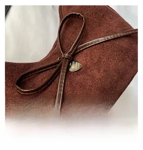Detail of brown suede underarm bag with leather bow and heart-shaped metal pendant