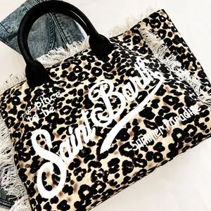 Detalle de bolso tote de lona con estampado de leopardo, flecos blancos y asas de cinta