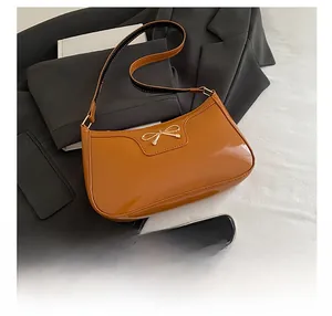 Detail of glossy brown patent leather baguette bag with a golden bow metal clasp