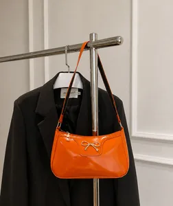 Détail du sac baguette en cuir verni orange brillant avec boucle métallique à nœud