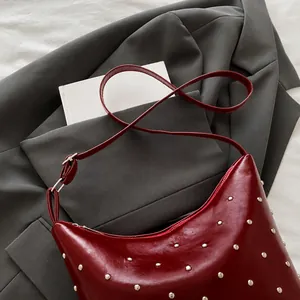 Detail of burgundy leather crescent bag with silver metal studs and thin shoulder strap