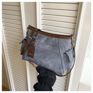 Detail of blue denim bucket bag with brown leather trim and fashion tag held by hand