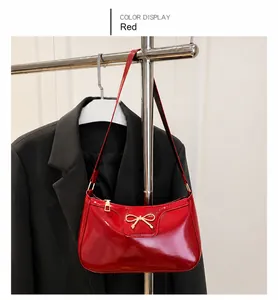 Détail du sac sous le bras en cuir verni rouge avec nœud métallique doré et zip