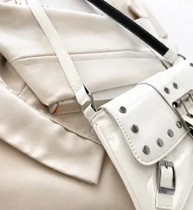 Close-up of white patent leather shoulder bag with silver rivets and metallic buckle details