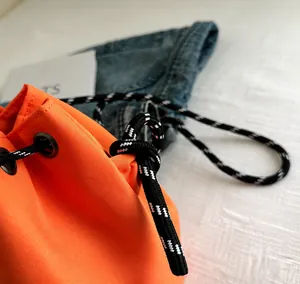 Primer plano de bolso cubo de nylon naranja con cordon trenzado y ojales metalicos