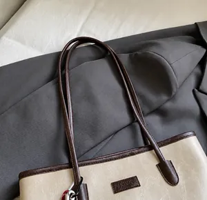 Close-up of contrast brown handles and refined stitching on beige tote shoulder bag
