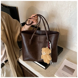 Detail of dark brown tote bag with leather texture and cute plush bear charm accessory