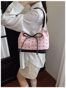Détail du sac à bandoulière rose à texture froissée avec nœud noir et liseré contrasté