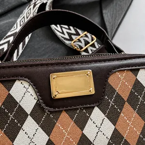 Macro detail of plaid knit fabric with leather trim and gold metal logo plaque