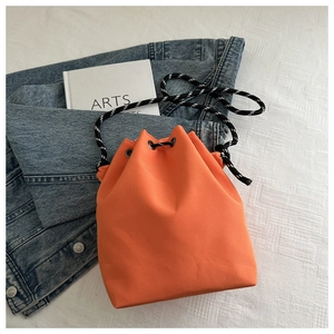 Détail du sac seau en nylon orange avec fermeture à cordon et bandoulière tressée