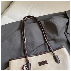 Detail of beige tote bag with litchi texture and brown straps on a grey suit