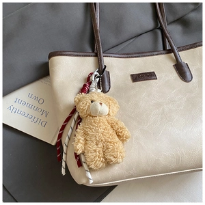 Detail of a brown teddy bear plush charm with knot on a cream faux leather tote bag