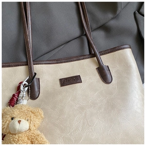 Detail of beige tote bag with litchi texture, fashion label and plush bear charm