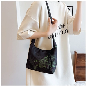 Detail of black crescent shoulder bag featuring a vivid green leaf print and zipper closure