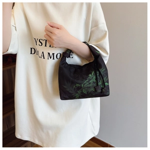 Detail of black crescent bag with green leaf print and stylish knotted strap design