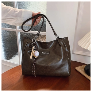 Detail of dark brown leather tote bag featuring a baseball charm and fashion tag
