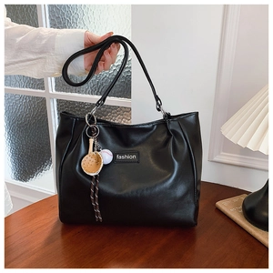 Detail of black PU leather tote bag with sport charms on a dark wood table