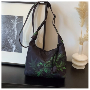Detail of black crescent shoulder bag with green leaf print and adjustable buckle strap