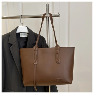 Detail of a brown leather tote bag showing the fashion logo and large capacity structure