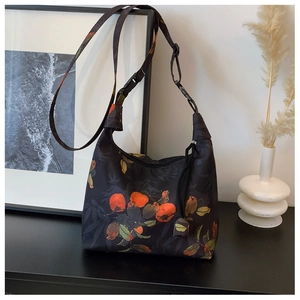 Detail of black crescent crossbody bag with orange persimmon print and adjustable strap