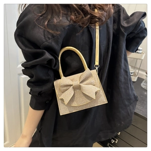 Dettaglio di una mini borsa dorata glitterata con fiocco indossata su una camicia