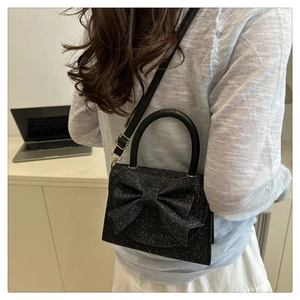 Vista laterale della borsa nera glitterata con grande fiocco portata a spalla da modella