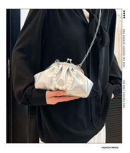 Detail van zilveren geplooide cloud bag met parelhandvat en metalen schouderketting