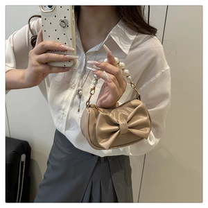 Detail van een beige tas met strik, parelhandvat en chique metalen sluiting erop