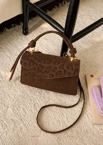 Détail du sac léopard avec poignée nouée et ferrures dorées sur un tapis blanc