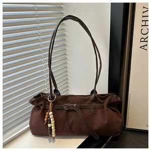 Detail of dark brown suede tote bag featuring a beaded tassel and metal buckle strap