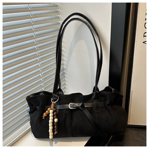Close-up of black faux suede tote bag featuring ethnic wooden bead tassel and metal buckle