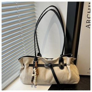 Detail of beige suede tote bag with black strap and decorative beaded charm accessory