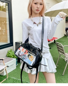 Detail of black ita bag with clear window showing anime character cards outdoors