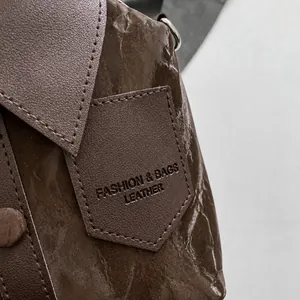 Détail du sac à main marron foncé montrant la texture plissée et les patchs logo embossés
