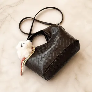 Detailed top view of a dark brown woven leather tote bag with a cute plush bear charm