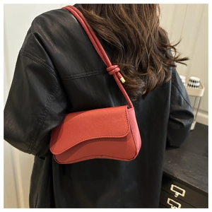 Detail van rode schoudertas met asymmetrische flap en geknoopte lederen riemdetails