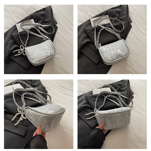 Detail of grey crossbody bag with silver chain handle and decorative pearl bow charm