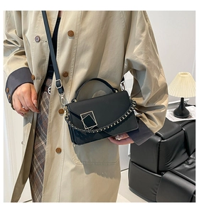 Detail view of black crossbody bag with gold buckle and woven chain on beige trench coat
