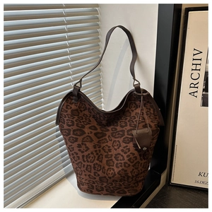 Detail of leopard print tote bag featuring brown leather straps and hanging charm ornament