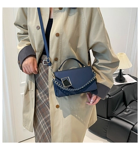 Detail of navy blue crossbody bag with geometric metal buckle and woven chain strap