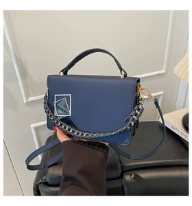 Detail of navy blue shoulder bag with gold geometric buckle and woven chain handle