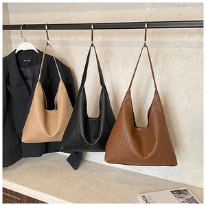 Three woven leather hobo shoulder bags in beige, black, and tan hanging on a metal rack