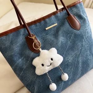 Detail of blue denim tote bag with brown leather trim and cute plush cloud pendant